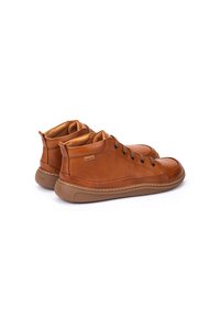 Zapatillas altas de cuero marrón con punta redonda, costuras en contraste y siete ojales. Suela de goma para tracción y comodidad.