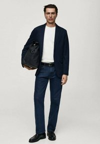 Sacou bleumarin peste un tricou alb, blugi de culoare bleumarin închis, pantofi negri și o geantă neagră. Sacoul are o croială ajustată și rever în formă de v.