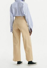 Un pantalon beige à jambes larges associé à une chemise rayée bleu et blanc. Le pantalon est en coton et dispose de deux poches arrière.