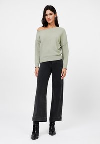Lysegrønn, overdimensjonert strikket genser med av-skulder design, kombinert med høytlivde, vide svarte jeans og svarte ankelboots.