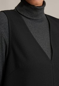 Μαύρο γιλέκο με ρίγες σε στρώσεις πάνω από γκρι, ραμμένο μπούστο με ζιβάγκο. Απαλή ύφανση με σχέδιο V στην λαιμόκοψη και κεκλιμένα ράψιματα στους ώμους.