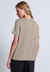 Beige kortärmad T-shirt med avslappnad passform, med rundad krage och mjuk textur. Bärs med svarta byxor.