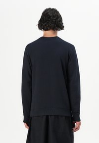 Felpa blu scuro con maniche lunghe, polsini a costine e scollatura a girocollo. Realizzata in tessuto morbido, presenta un design pulito e minimalista.