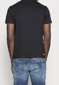 Svart bomull t-shirt med kort ärm, med en enkel design. I kombination med blå denimjeans, som visar en klassisk passform och synlig sömnad.