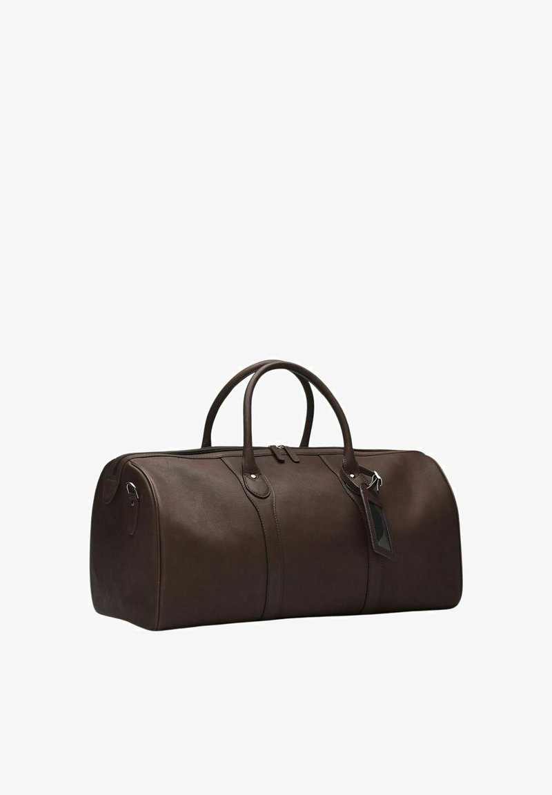 Ruskea nahkainen duffel-laukku, jossa on kaksi pyöreää kahvaa, vetoketjukiinnitys ja matkatavaratunniste. Sileä rakenne ja pyöreä muoto, jossa on hienovaraisia ompeluyksityiskohtia.