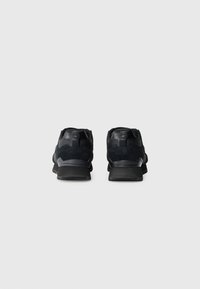 Chaussures de sport noires avec un mélange de matériaux lisses et texturés, dotées d'un talon renforcé, d'une semelle en caoutchouc et d'un design minimaliste.