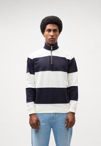 Felpa a strisce blu navy e bianca con colletto alto, zip a un quarto e polsini a costine. Realizzata in tessuto morbido con una vestibilità casual.