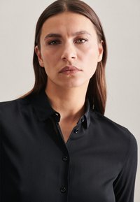 Camicia nera con colletto, caratterizzata da una texture liscia e bottoni neri lucidi lungo la parte anteriore.