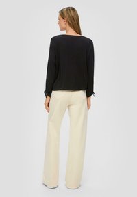 Schwarzes Longsleeve-Oberteil mit lockerer Passform und gebundenen Ärmeln, kombiniert mit cremefarbenen, weit geschnittenen Hosen, die über eine weiche Textur und neutrale Töne verfügen.