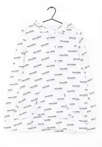 Vit hoodie med svart textmönster "HOLLISTER", framficka, dragsko vid huvan och ribbad nederkant. Tillverkad av mjukt och bekvämt material.