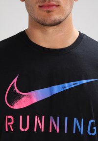Černé bavlněné tričko s růžovo-modrým p řechodem loga Nike Swoosh a výrazným nápisem "RUNNING" v kontrastním fontu níže.