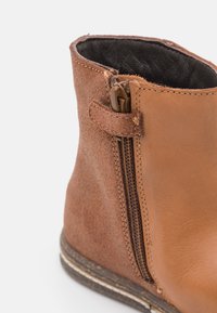 Bottine en cuir marron avec une finition en daim texturé, fermeture éclair latérale et couture contrastante. Semelle en caoutchouc avec une bordure brun clair.