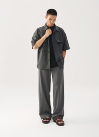 Siva majica kratkih rukava s dvije prednje džepove, preko crne majice. Sive hlače širokog kroja i smeđe sandale na remenčiće upotpunjuju outfit.