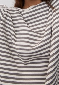 Femme portant un t-shirt à manches longues rayé horizontalement gris et blanc, à encolure ronde, raccourci pour montrer les épaules et le haut de la poitrine.