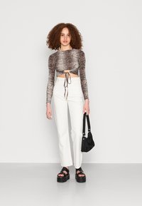 Top cropped de mangas longas com um padrão de riscas pretas e castanhas, jeans brancos de cintura alta e sandálias de plataforma pretas, acompanhados de uma bolsa preta.