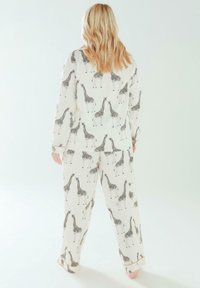 Set di pigiama bianco con stampa di giraffe nera. Maglietta comoda con maniche lunghe e pantaloni abbinati, tessuto leggero con una superficie liscia.