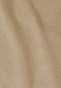 Tissu beige texturé avec une surface douce rappelant le daim, présentant de légères ondulations et plis. Matériau léger et flexible.
