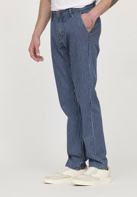 Pantalons rayés bleus en tissu léger, avec une coupe droite et des poches avant, associés à des baskets blanches.
