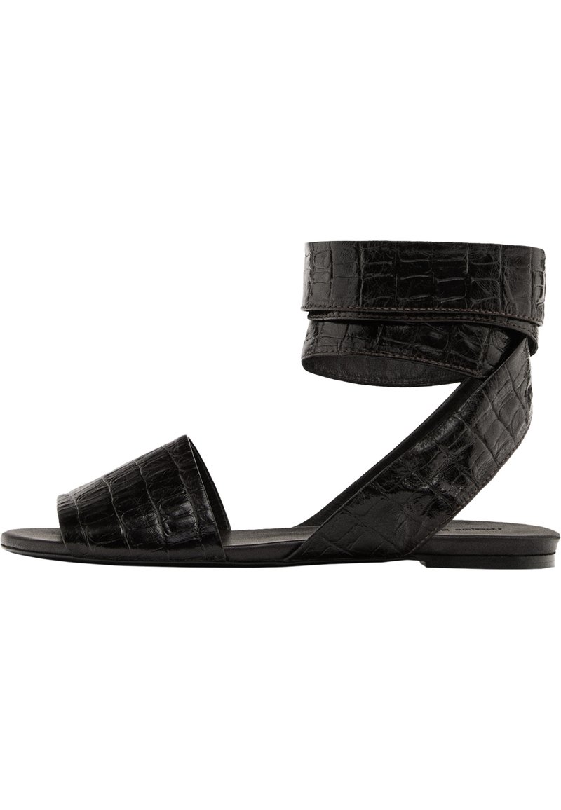 Schwarze flache Sandalen mit Krokodilprägung, offener Zehenpartie und Knöchelriemen. Sie verfügen über einen breiten Zehenriemen und ein schlankes, minimalistisches Design.
