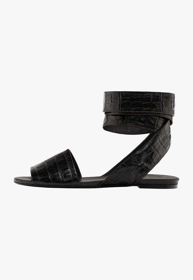 Zwarte platte sandalen met een krokodillenstructuur, open teen en enkelbandje. Kenmerken zijn een brede teenband en een strakke, minimalistische uitstraling.