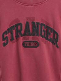 Sudadera roja con texto bordado en negro "STRANGER" y "THINGS". Tejido suave y texturizado; cuello y puños acanalados. Diseño clásico de cuello redondo.