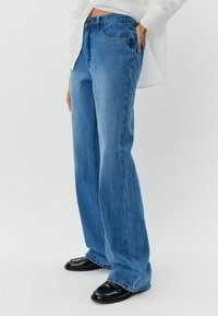 Plave široke traperice s srednje visokim strukom, s kopčanjem na dugme, pet džepova i suptilnim detaljima šivanja.