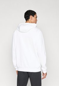 Λευκό φούτερ με κουκούλα και κορδόνι, με ριμπ μανσέτες, κατασκευασμένο από μαλακό υλικό. Ξεχωρίζει για τον καθαρό, μίνιμαλ σχεδιασμό και τη χαλαρή εφαρμογή.