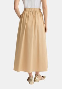 Gonna beige lunghezza caviglia realizzata in tessuto liscio, con vita elastica e vestibilità morbida. Abbinata a scarpe basse dorate e lucide.