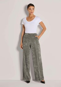 Graue Cordhosen im weiten Schnitt mit vertikalen Streifen, kombiniert mit einem enganliegenden weißen Kurzarmoberteil. Die Schuhe sind schwarz mit spitzen Zehen.