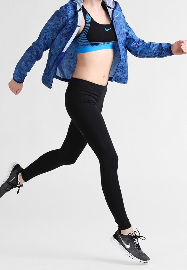 Vêtements de sport Nike comprenant une veste à motifs bleus, un legging noir et un soutien-gorge de sport bleu, accompagnés de chaussures de course grises.