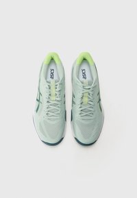 Baskets de sport vert clair en matière mesh, avec lacets intégrés et une touche de vert. Présentent une surface texturée et une semelle contrastante en bleu marine.