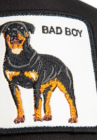 Gorra negra con un parche blanco que presenta un Rottweiler bordado en negro y naranja. Texto "CHICO MALO" encima del perro.