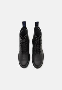 Svarta läderankelstövlar med snörning, rund tå, platt sula och dragöglor. Slät textur med subtila sömnadsdetaljer.
