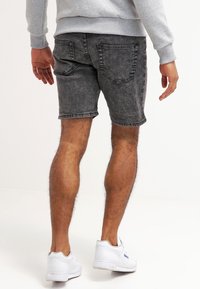 Pantalones cortos de mezclilla negra con una textura desvanecida, de longitud a mitad del muslo y diseño de cinco bolsillos. Combinados con una sudadera gris y zapatillas blancas.