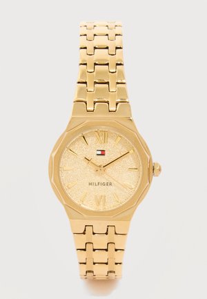 Goudkleurig Tommy Hilfiger horloge met een gestructureerde wijzerplaat, Romeinse cijfers, logo om 12 uur en een metalen armband met schakels.
