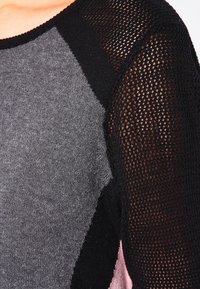 Stickad tröja med grå och rosa paneler och svarta meshärmar. Tyget är mjukt med en kontrasterande texturerad design.