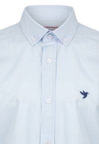 Camisa de botones azul claro con un cuello afilado, con botones blancos y un logo de pájaro bordado en color marino en el lado izquierdo del pecho. Textura de tela suave.