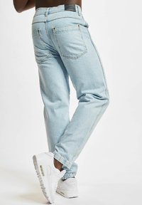 Light blue denim jeans with a relaxed fit, featuring back pockets and contrast stitching. Paired with white athletic shoes.