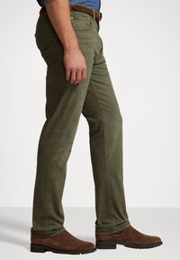 Pantalones de pierna recta en verde oliva, confeccionados con una mezcla de algodón. Presentan un diseño clásico de cinco bolsillos y detalles de costura sutiles.