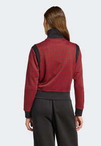 Röd och svart kort jacka med ett hundtandsmönster, hög krage samt elastiska ärmslut och nederkant, tillverkad av mjukt, texturerat tyg.