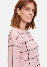 Heller rosa Pullover mit einem Karomuster aus schwarzen Linien, aus weichem Stoff gefertigt; runder Ausschnitt, lange Ärmel und lässige Passform.