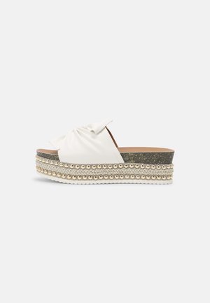 Hvid slip-on platform sandal med knyttet overdel, korksål, fletdetalje af jute og guldbedeudsmykning på mellemsålen.