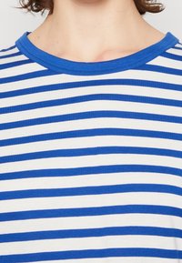 Randig t-shirt med blå och vita horisontella ränder, ribbad blå halsringning, mjukt bomullsmaterial och klassisk rundhalsad design.