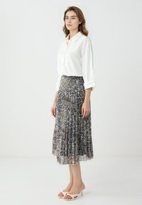 Weißes Hemd mit hochgeschlagenen Ärmeln, kombiniert mit einem plissierten knöchellangen Rock im Schlangenmuster in Grautönen und Schwarz.