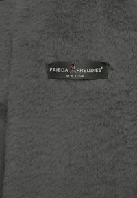 Szary materiał z sztucznego futra o miękkiej teksturze, z czarną i czerwoną metką "Frieda Freddies, New York" wyraźnie widoczną.