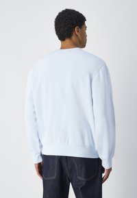 Sudadera azul claro de manga larga, con cuello redondo, puños y dobladillo acanalados. La tela parece suave y con una textura lisa.