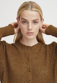 Rjava pletena cardigan jakna z teksturirano, zigzag vzorcem, okroglo ovratnikom in gumbnim zapiranjem spredaj. Pulover ima dolge rokave.