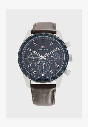 Montre-bracelet homme avec cadran bleu foncé, boîtier argenté, bracelet en cuir marron, trois sous-cadrans et échelle tachymétrique sur la lunette, marque Hilfiger.