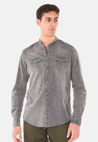 Camicia in denim grigia con colletto alla mandarino, due tasche sul petto, chiusura a bottoni e un leggero effetto sbiadito. Maniche lunghe con dettagli cuciti.