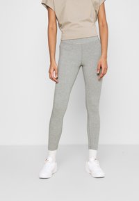 Grijze katoenen leggings met een aansluitend ontwerp, een gladde textuur en een lengte tot de enkels, gecombineerd met witte sneakers en een beige top.